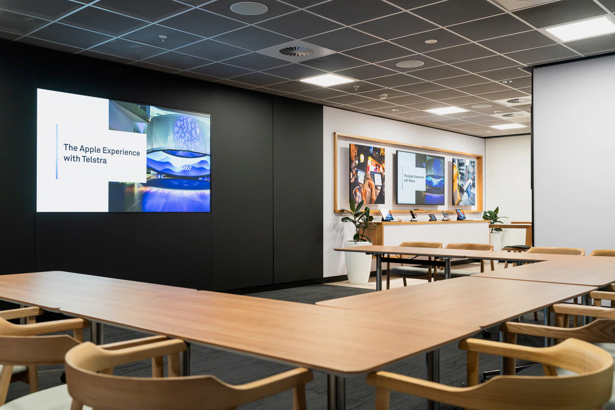Workshop room with timber tables, Apple devices and screens displaying The Apple Experience with Telstra